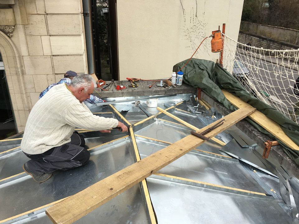 Ouvrier qui installe des tasseaux sur une zinguerie sous couverture