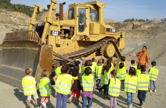 Un grupo de niños con chalecos amarillos están parados frente a una excavadora.