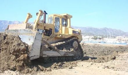 Una excavadora está moviendo tierra en un campo con montañas al fondo.