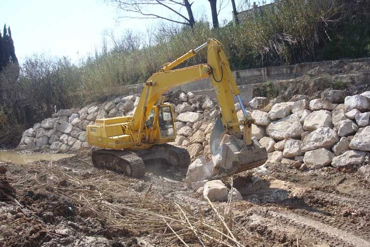 Una excavadora amarilla está moviendo rocas en un campo de tierra.