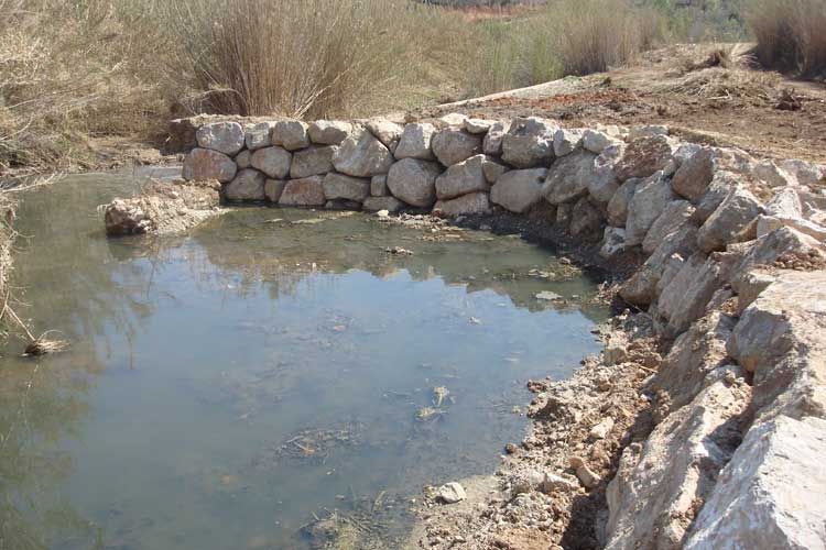 Un pequeño estanque rodeado de rocas en medio de un campo.