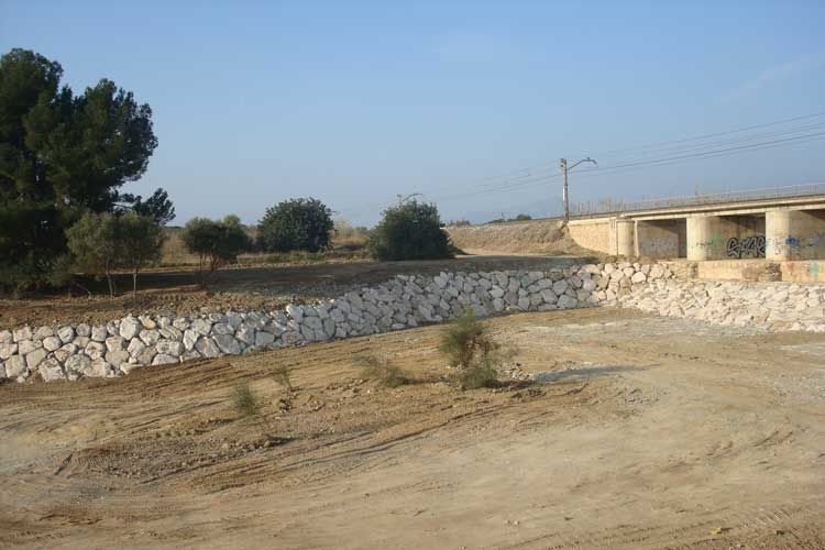 Hay un puente al fondo y un muro de piedra en primer plano.