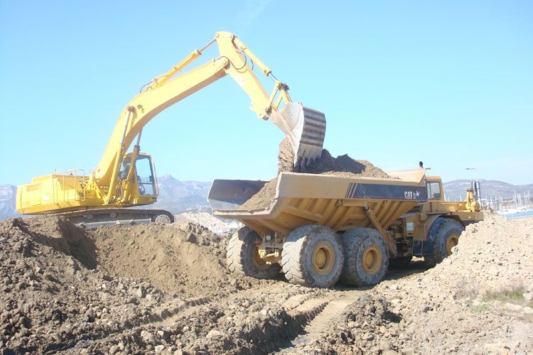 Una excavadora amarilla está cargando tierra en un camión volquete.