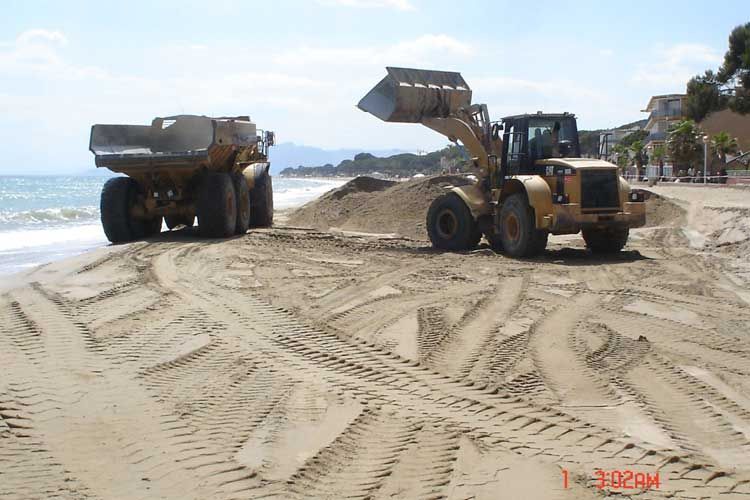 Una excavadora está cargando arena en un camión volquete en la playa