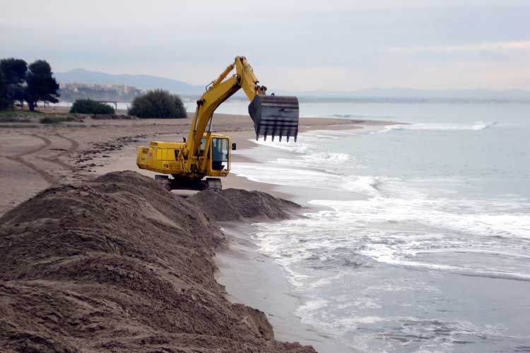 Una excavadora amarilla está trabajando en una playa cerca del océano.