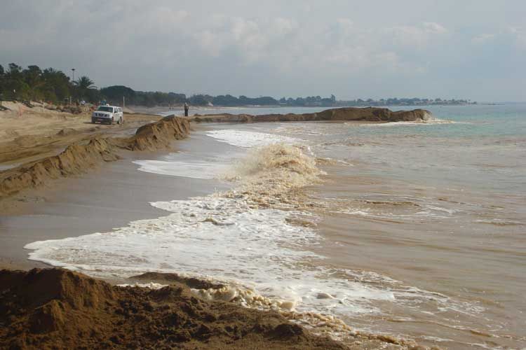 Un coche circula por un camino de tierra al lado de una playa.