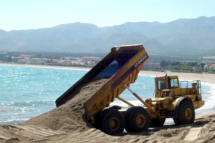 Un camión volquete está arrojando arena en una playa