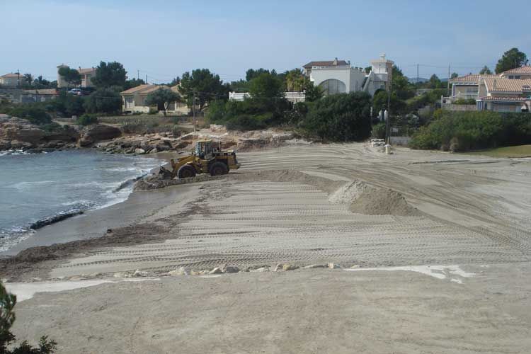 Una excavadora está trabajando en una playa cerca del océano.