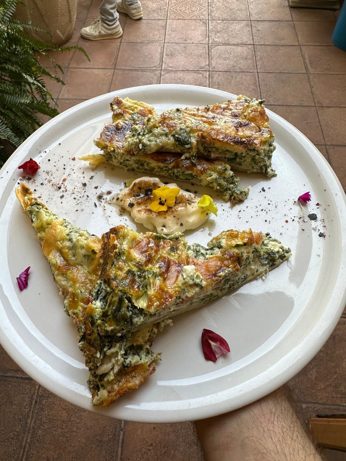 Tres porciones de pizza de verduras en un plato blanco sobre un suelo de baldosas al aire libre.