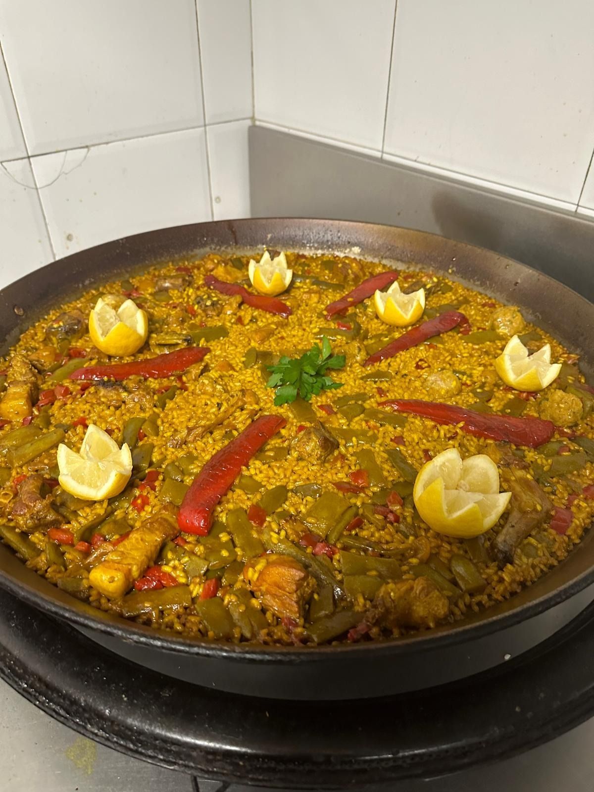 Una olla grande de arroz con azafrán, pimientos rojos y rodajas de limón sobre una estufa.