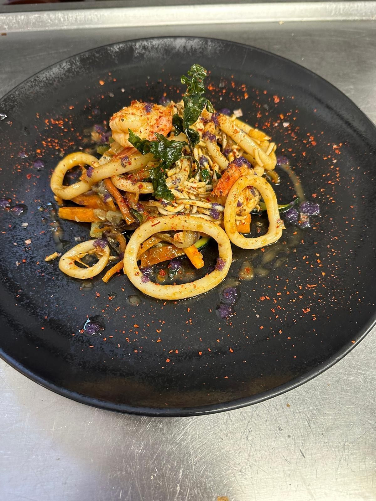 Plato de aros de calamar y gambas adornados con hierbas y especias sobre un plato negro.