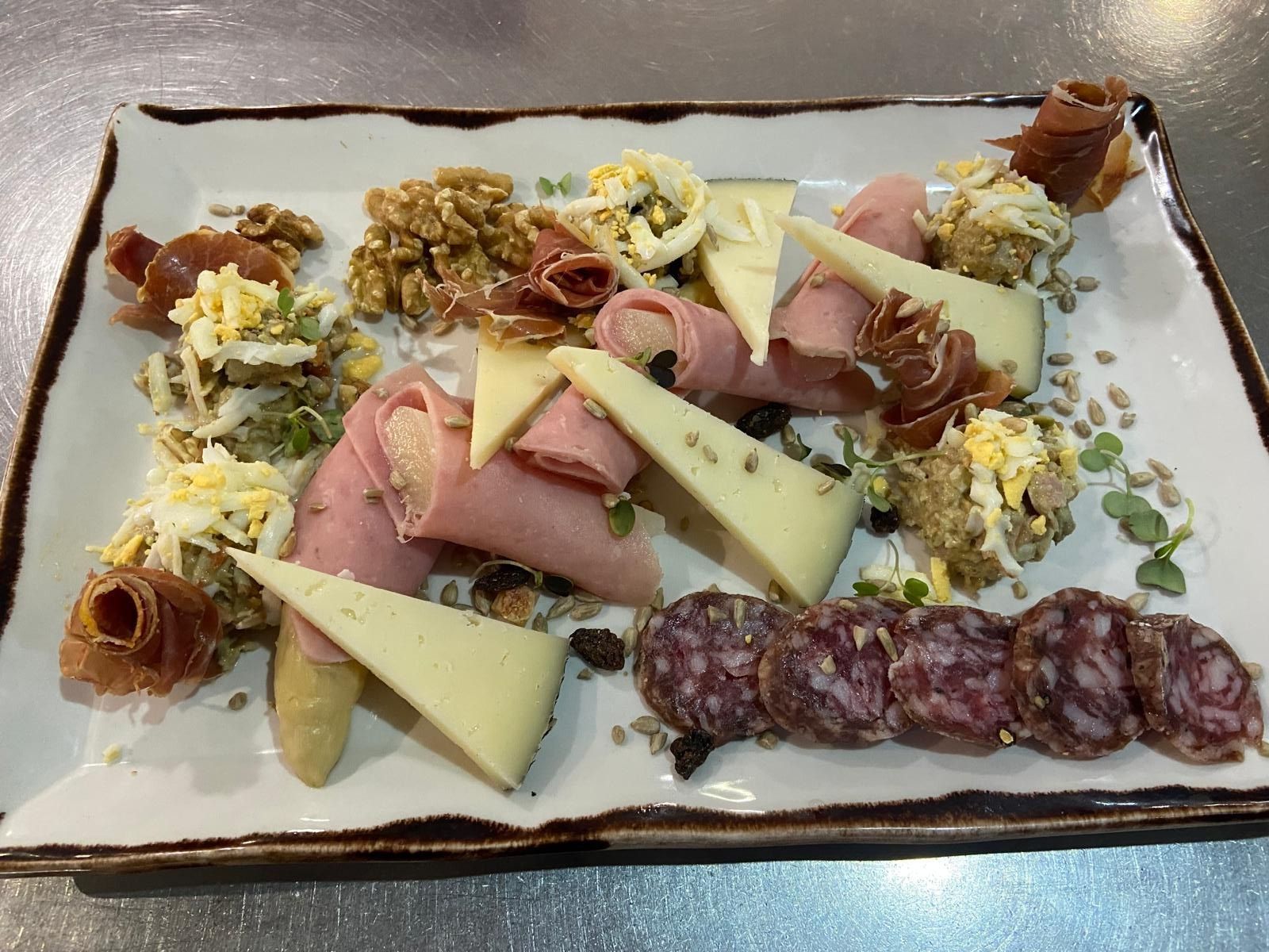 Surtido de embutidos en un plato rectangular con carnes, quesos y guarniciones.