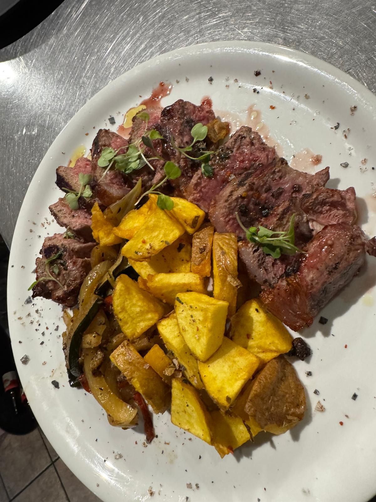 Filete emplatado con patatas asadas y hierbas en un plato blanco.