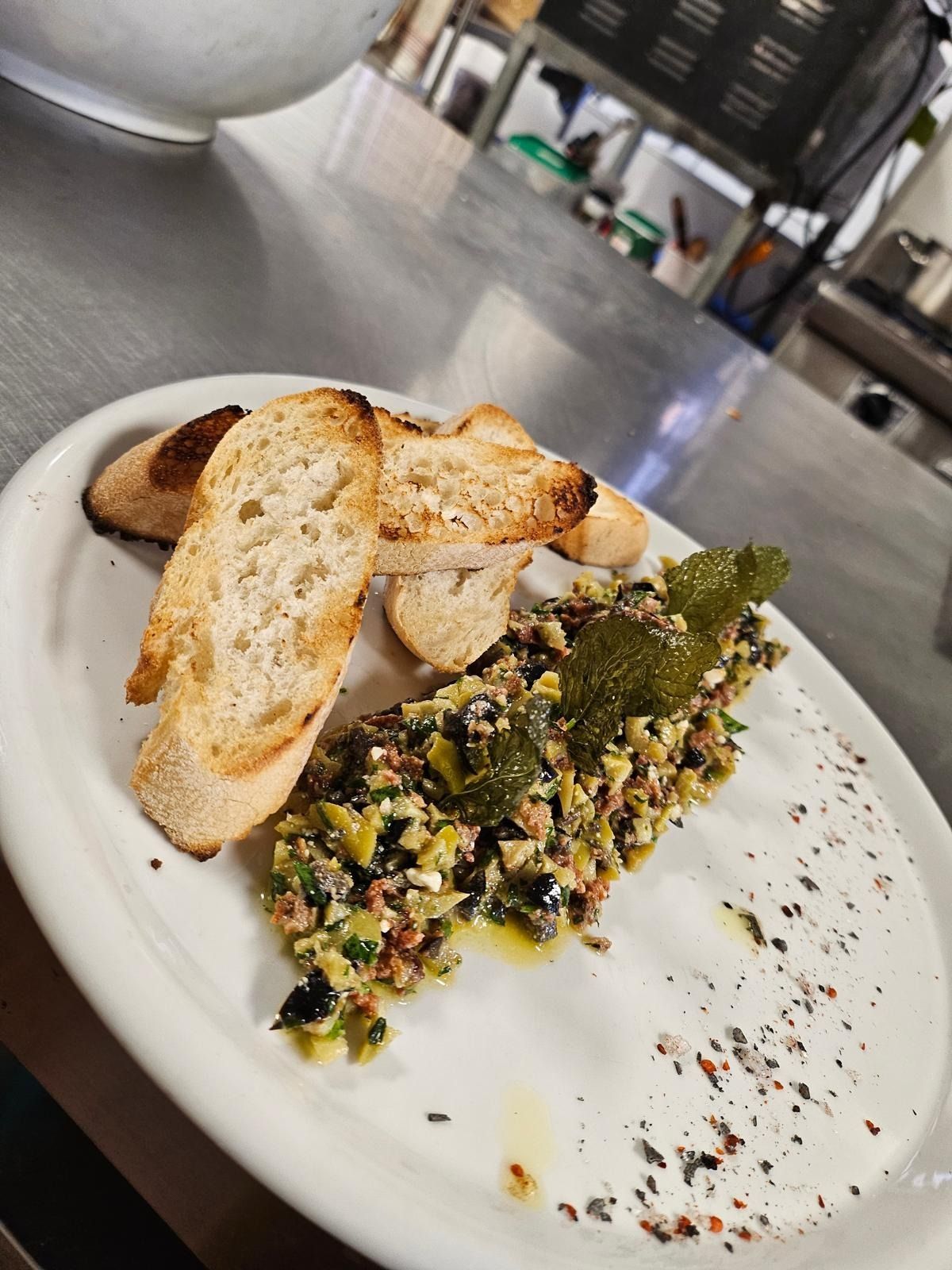 Plato con pan tostado y ensalada de cereales con hierbas aromáticas en un plato blanco en un entorno de cocina.