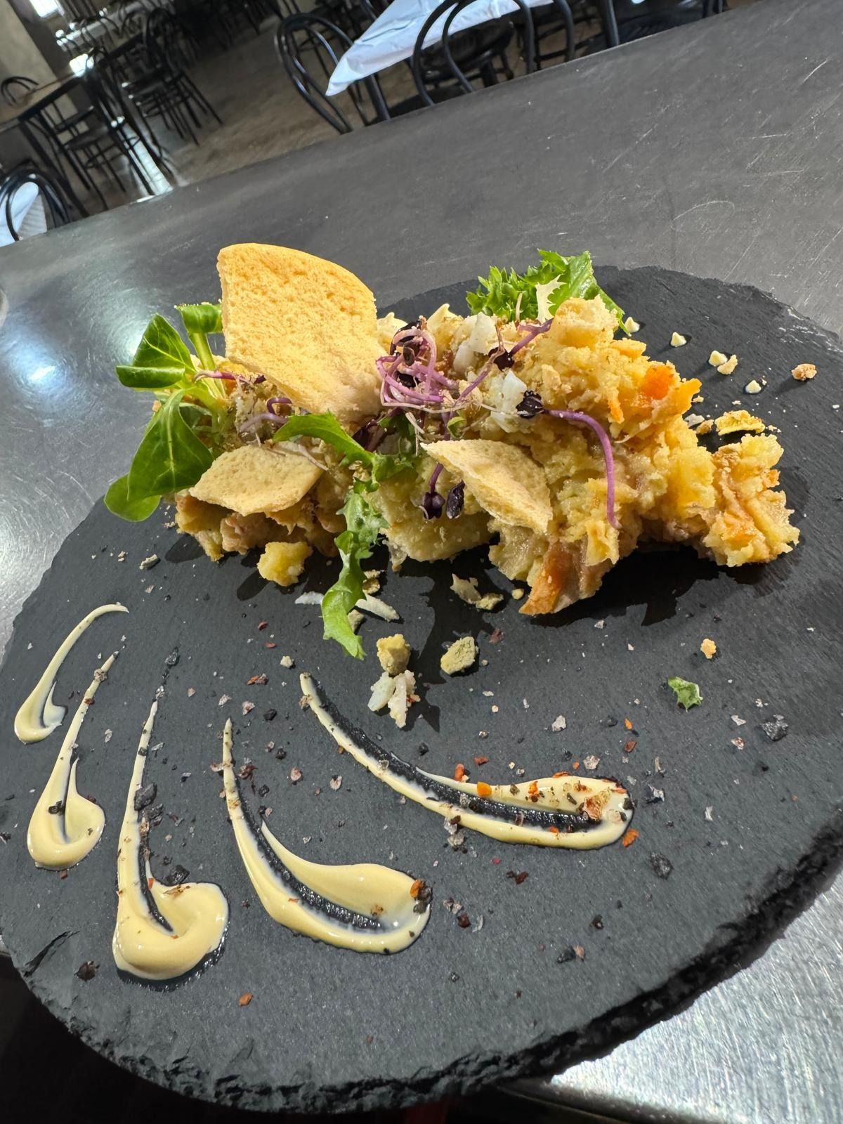 Plato negro con ensalada gourmet y remolinos de salsa sobre la mesa de un restaurante.
