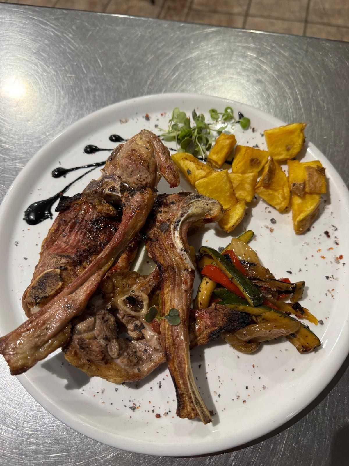 Chuletas de cordero a la parrilla con calabaza asada y verduras en un plato blanco con rociado de vinagre balsámico.