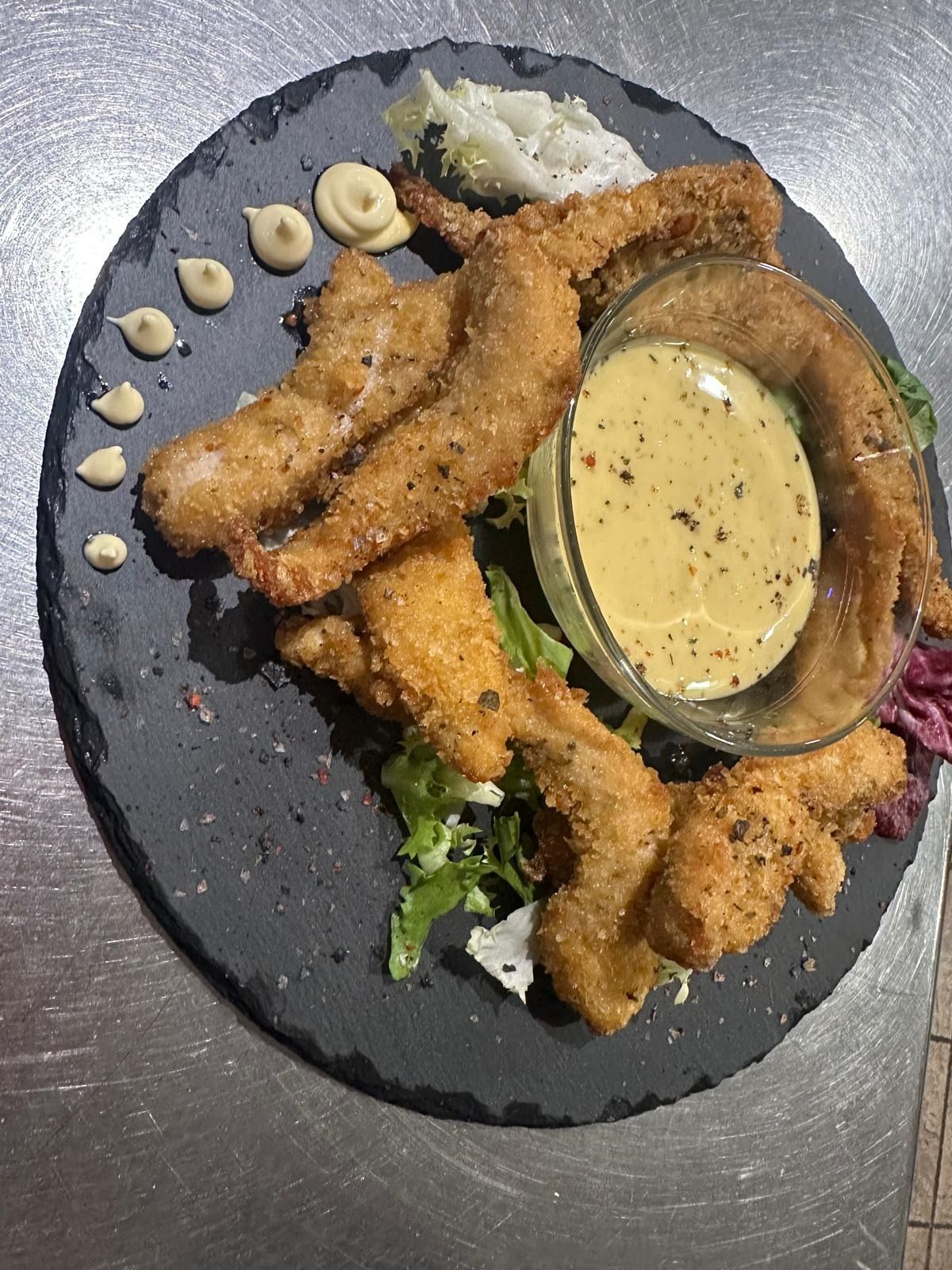 Camarones empanizados fritos en un plato negro con salsa para mojar y guarnición, servidos en una mesa.