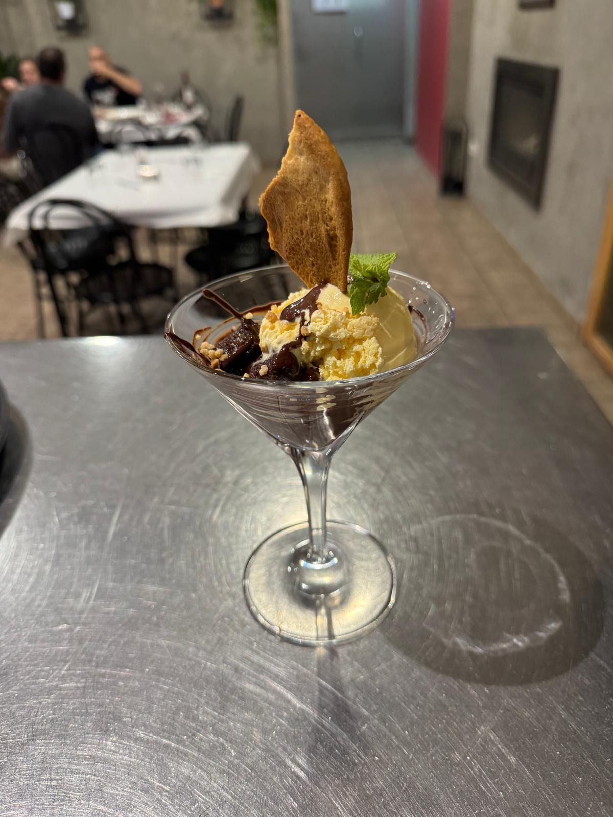 Postre en copa de martini con fruta y barquillo sobre una mesa de acero inoxidable en un restaurante.