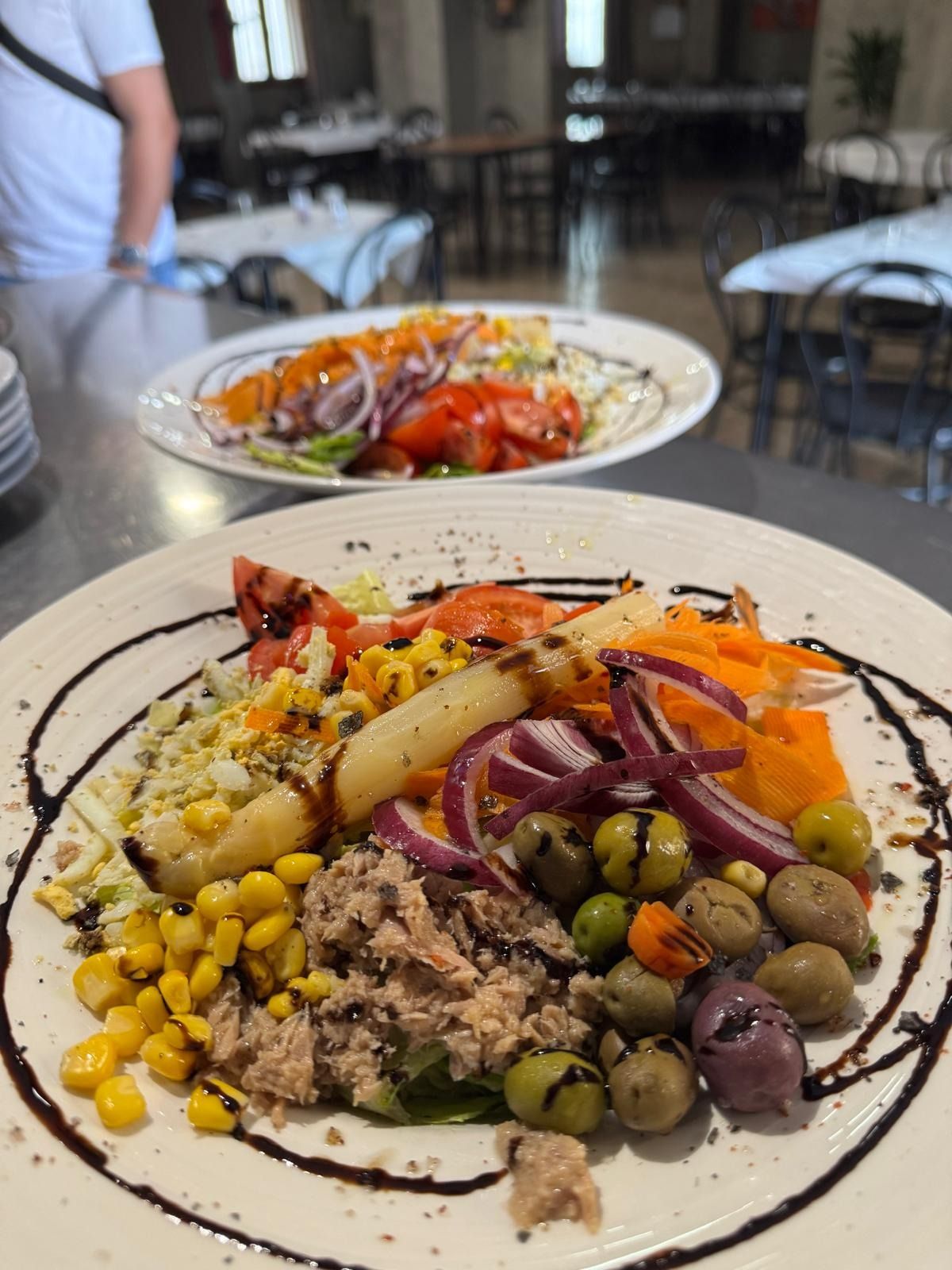 Plato de ensalada colorida con maíz, aceitunas, cebollas y verduras asadas en la mesa de un restaurante.