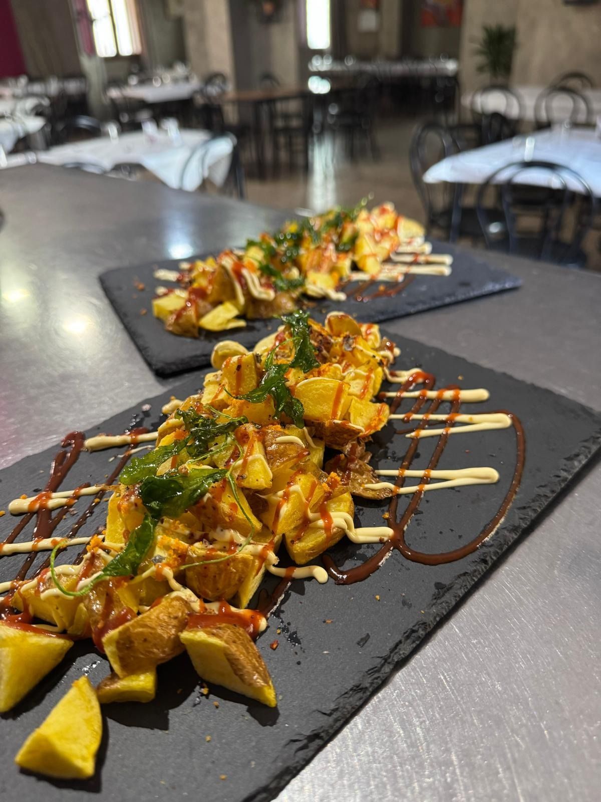En un restaurante, se muestran brochetas de aperitivos glaseados con hierbas, presentadas en bandejas negras.