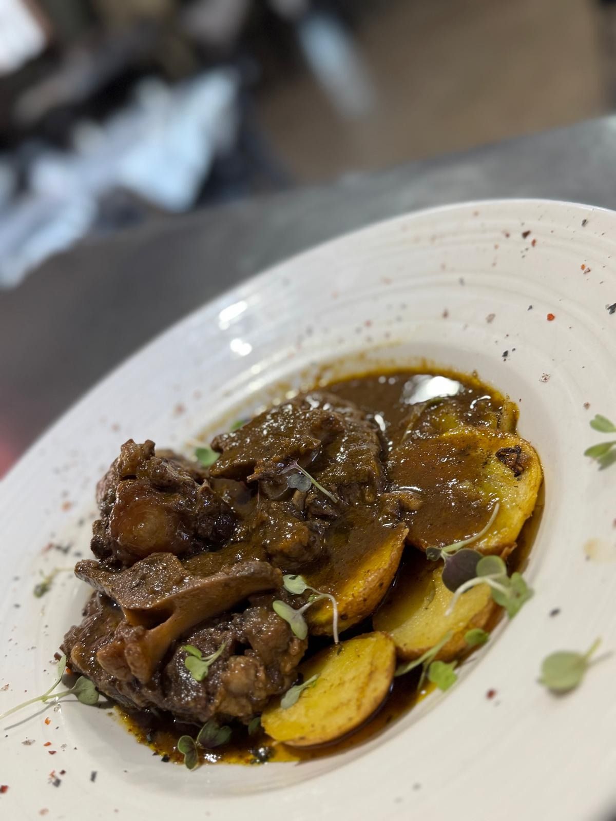 Plato de carne estofada y verduras en rodajas en salsa marrón sobre un plato blanco.