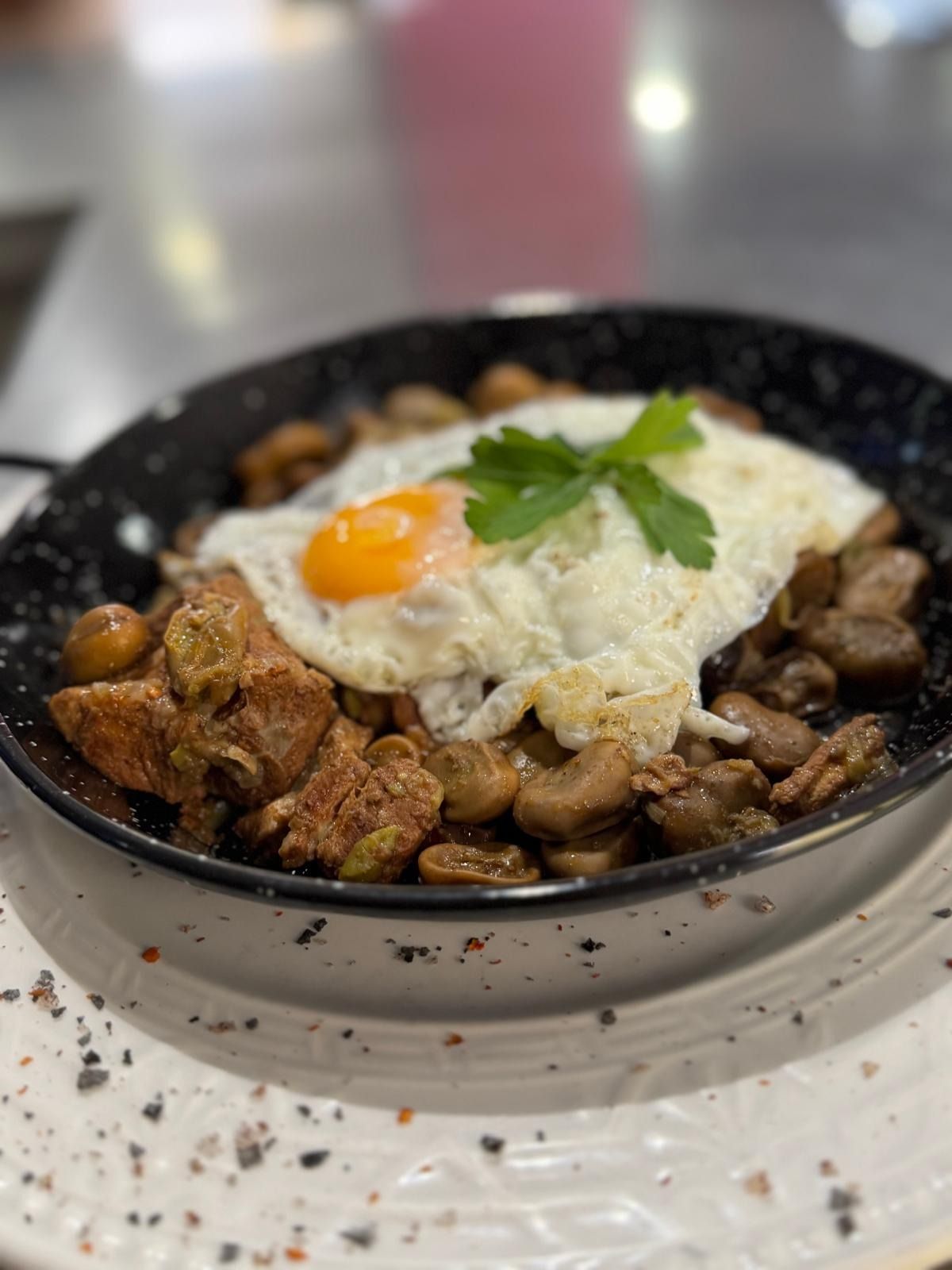 Un tazón negro de arroz cubierto con huevo frito y perejil sobre una mesa blanca.