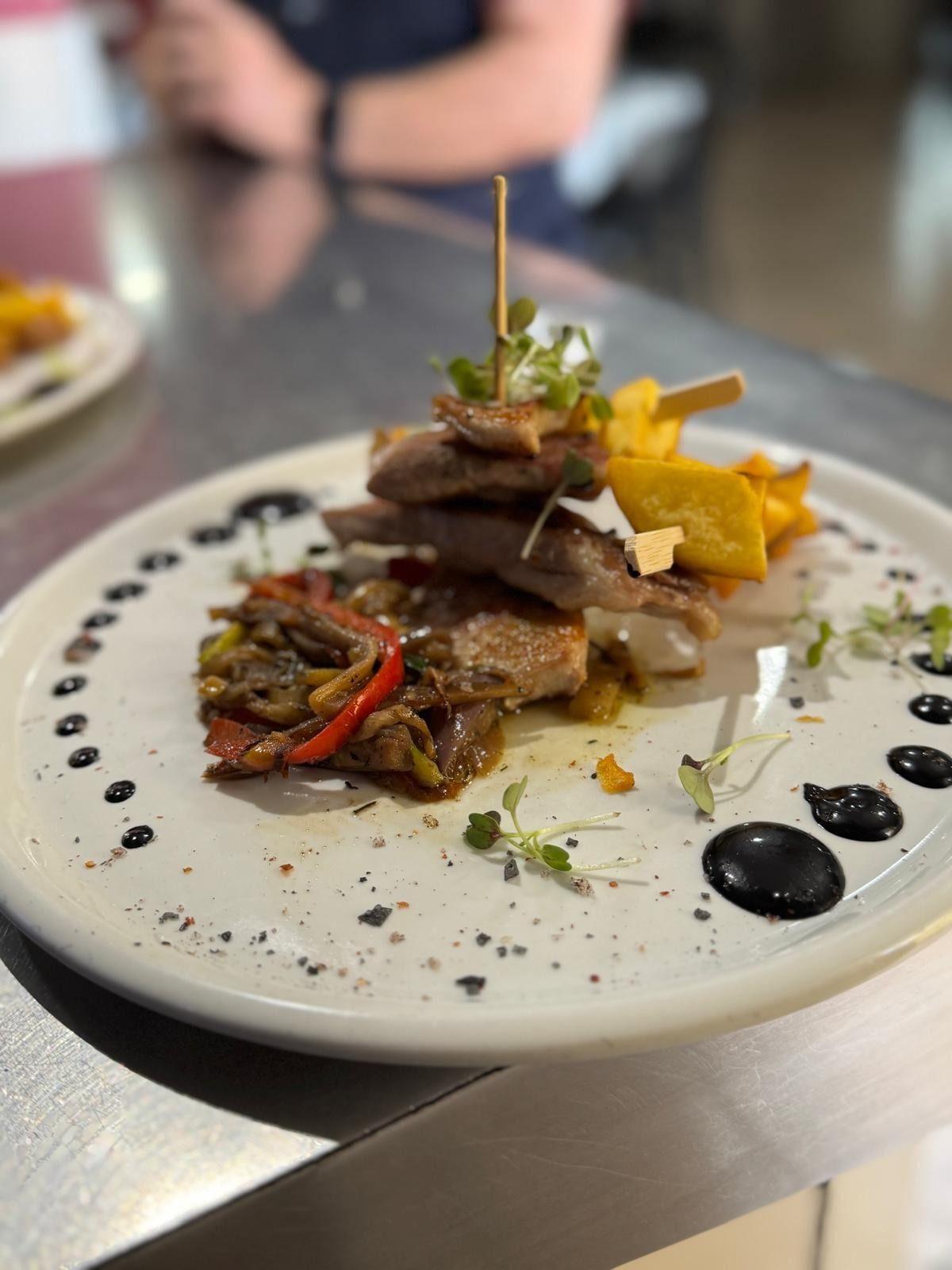 Plato gourmet de carne con puré amarillo y salsa servido en un plato blanco en un restaurante.