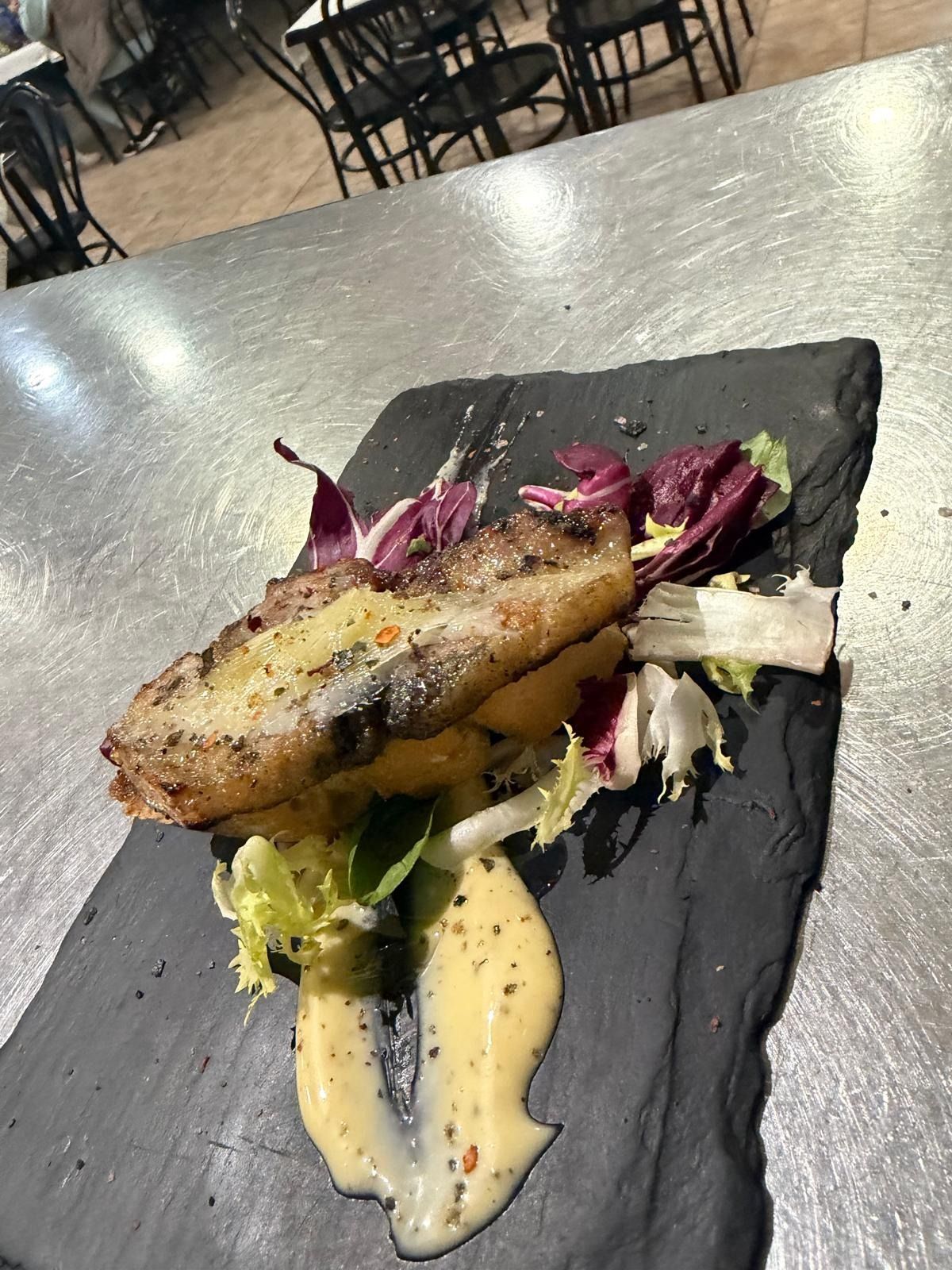 Filete de pescado a la parrilla sobre pizarra negra con verduras y salsa cremosa en una mesa de restaurante.