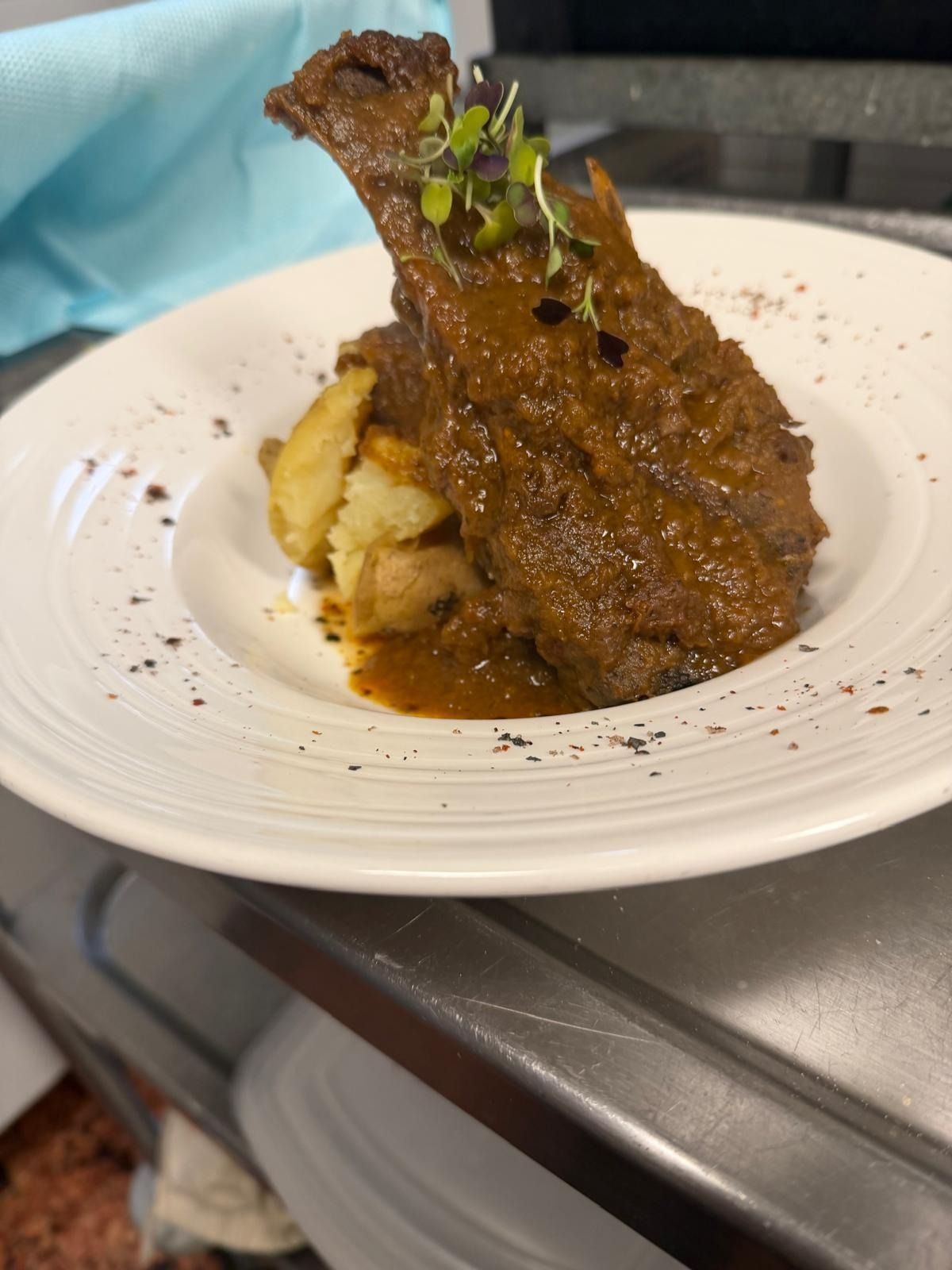 Carne sellada al plato, servida sobre puré de patatas y adornada con hierbas, en un plato blanco.