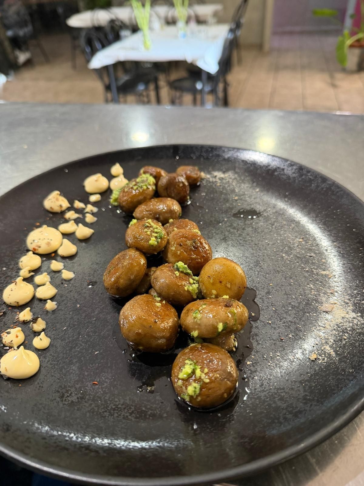 Plato negro de bolitas glaseadas del tamaño de un bocado con guarnición de pistacho y puntos de salsa