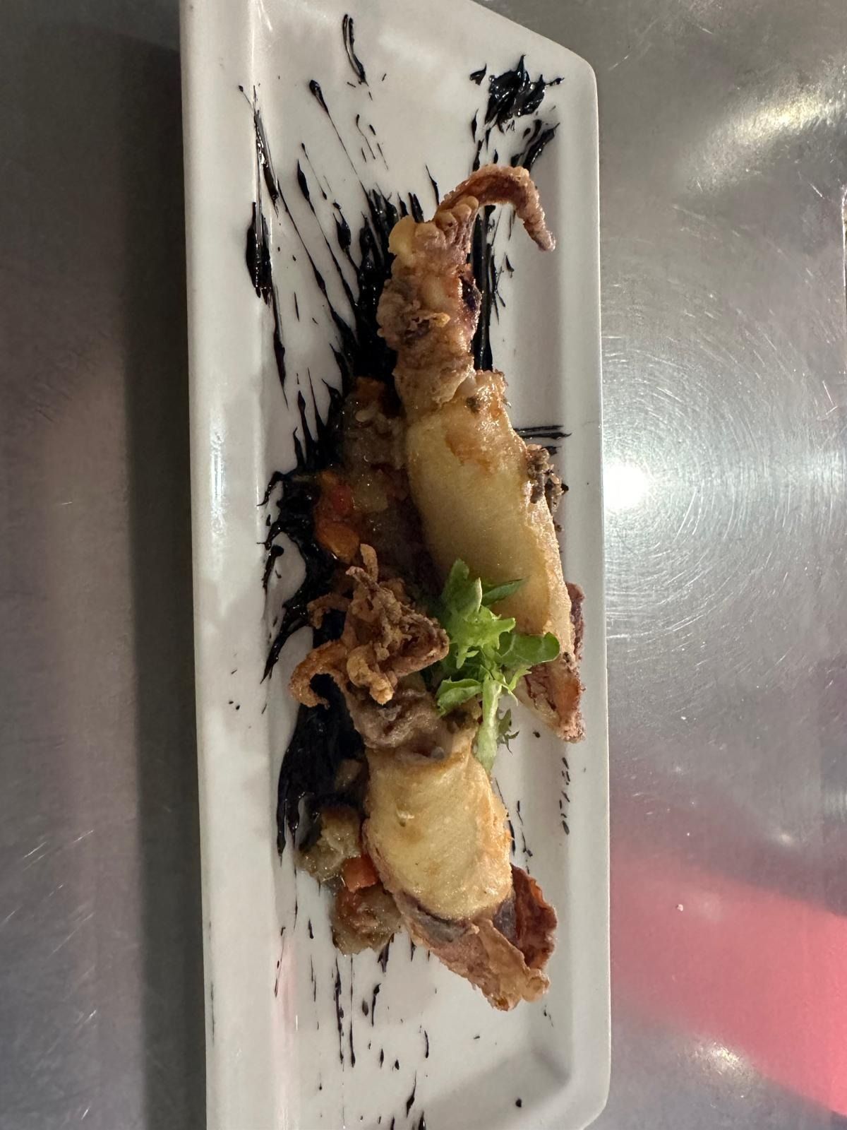 Plato de mariscos fritos con salsa y guarnición servido en un plato rectangular blanco.