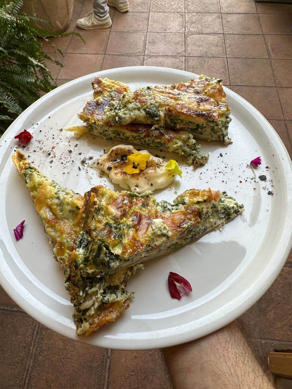 Plato con dos rebanadas de tortilla rellena de hierbas y una rodaja de limón sobre una mesa exterior de azulejos