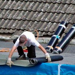Un hombre está trabajando en un techo con rollos de material para techos.