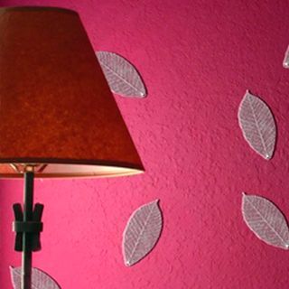 Una lámpara está delante de una pared rosa con hojas.