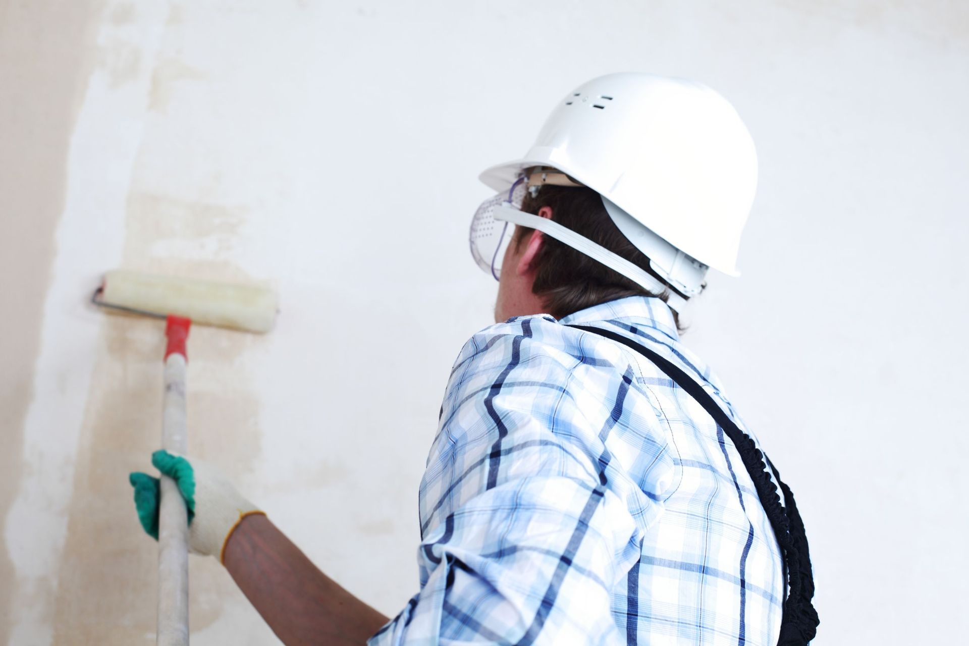 Un hombre que lleva un casco está pintando una pared con un rodillo de pintura.