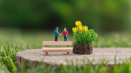 Zwei Miniaturmenschen geben sich auf einer Holzbank die Hand.