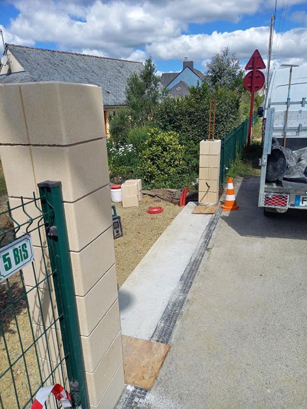 Chantier : piliers en béton en cours de construction près du portail vert et du camion de livraison.