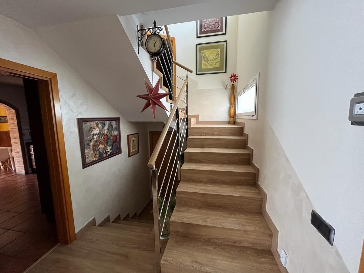 Escalera de madera con pasamanos metálico. Obras de arte y un reloj decoran las paredes.