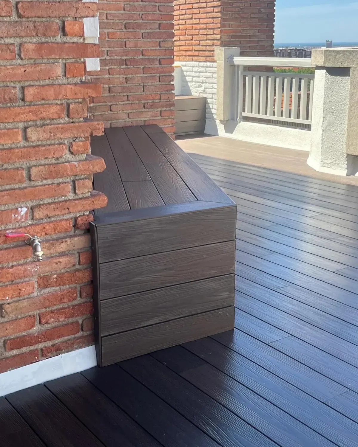 Banco de madera marrón empotrado en una esquina contra una pared de ladrillos en una terraza en la azotea.