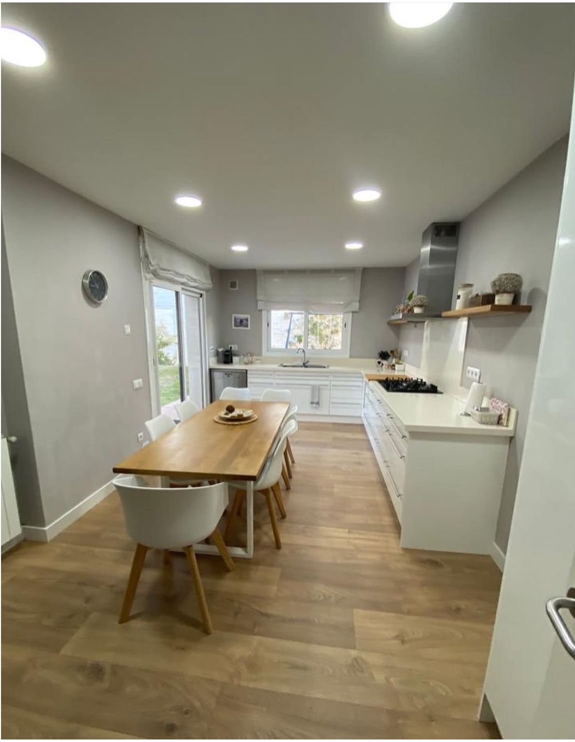 Cocina espaciosa y luminosa con pisos de madera, gabinetes blancos y una mesa de comedor de madera.