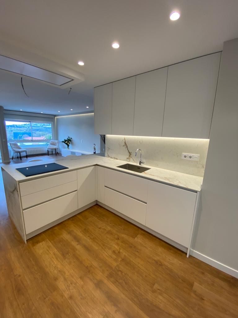 Cocina blanca moderna con isla, suelos de madera y electrodomésticos empotrados.