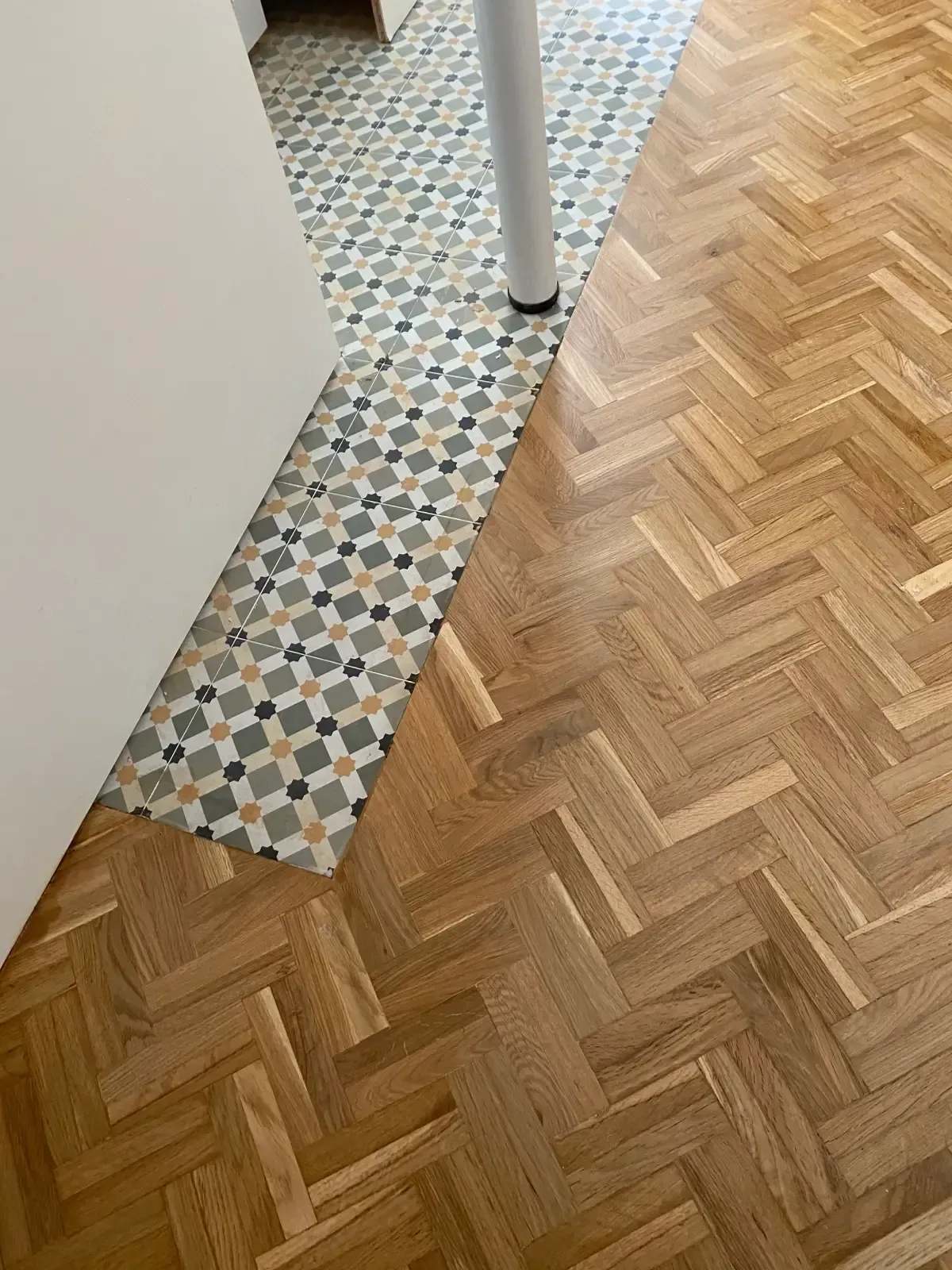 El piso de madera en espiga se combina con el piso de baldosas estampadas, en la transición a la altura de una puerta.