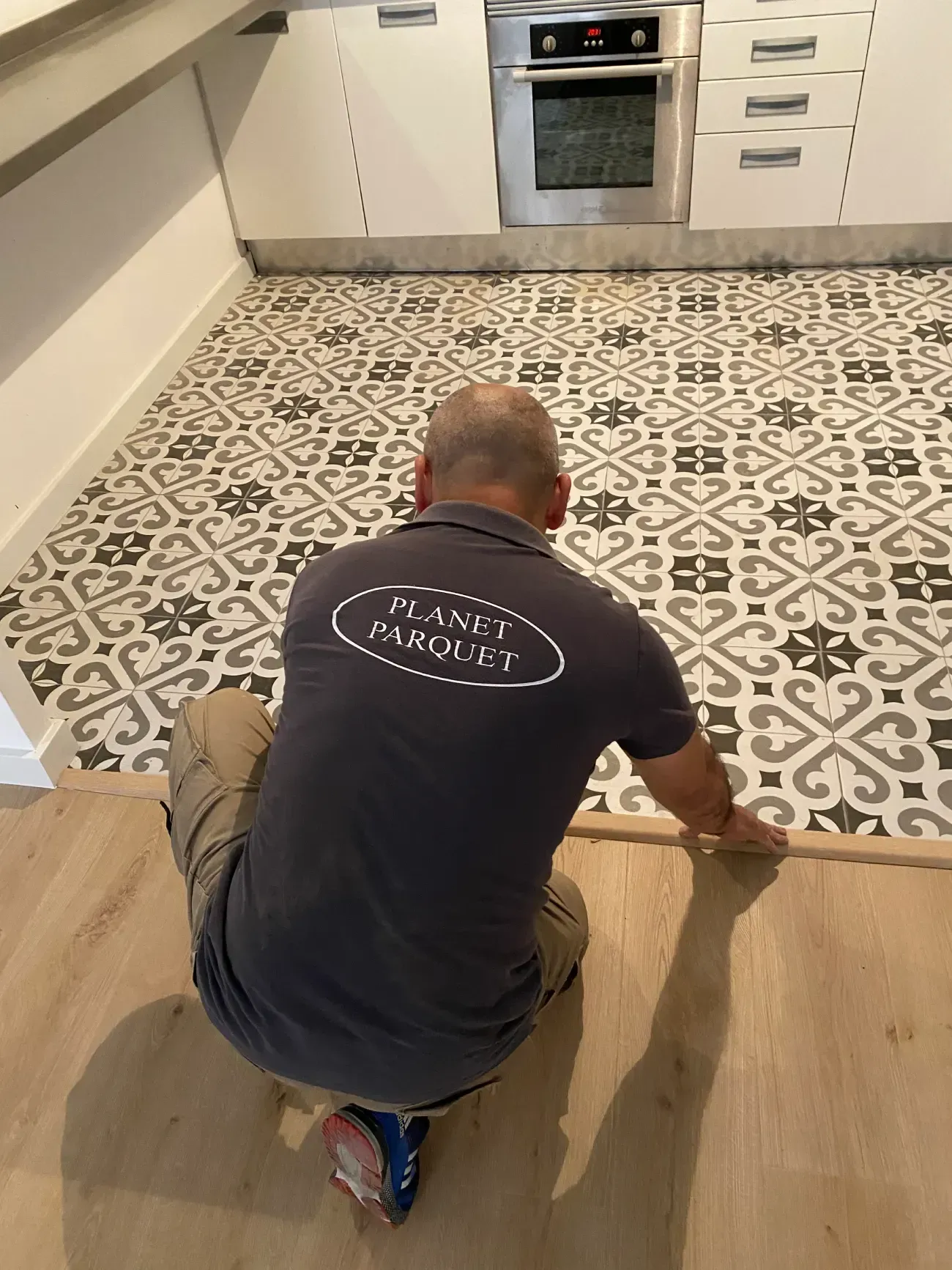 Persona arrodillada, instalando un piso de madera cerca del piso de la cocina con baldosas estampadas;