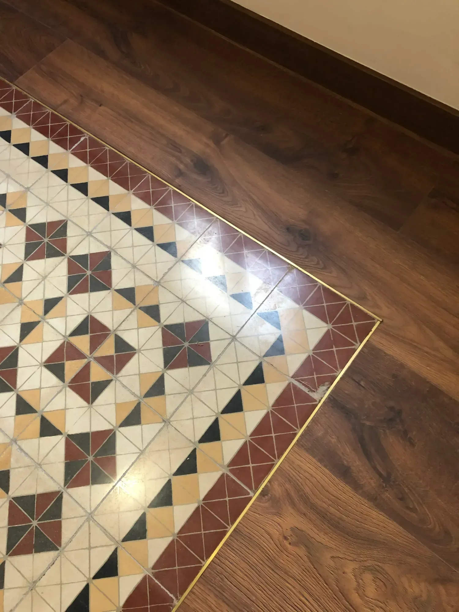 Un piso de baldosas con diseño geométrico se combina con un piso de madera, con una tira de latón en el medio.