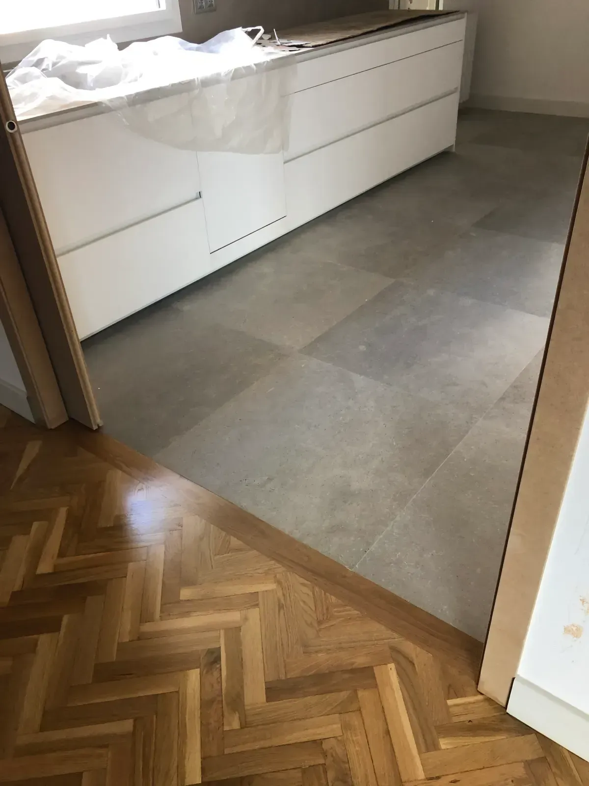 Un piso de madera en espiga se combina con un piso de baldosas grises en una entrada, al lado de gabinetes blancos.