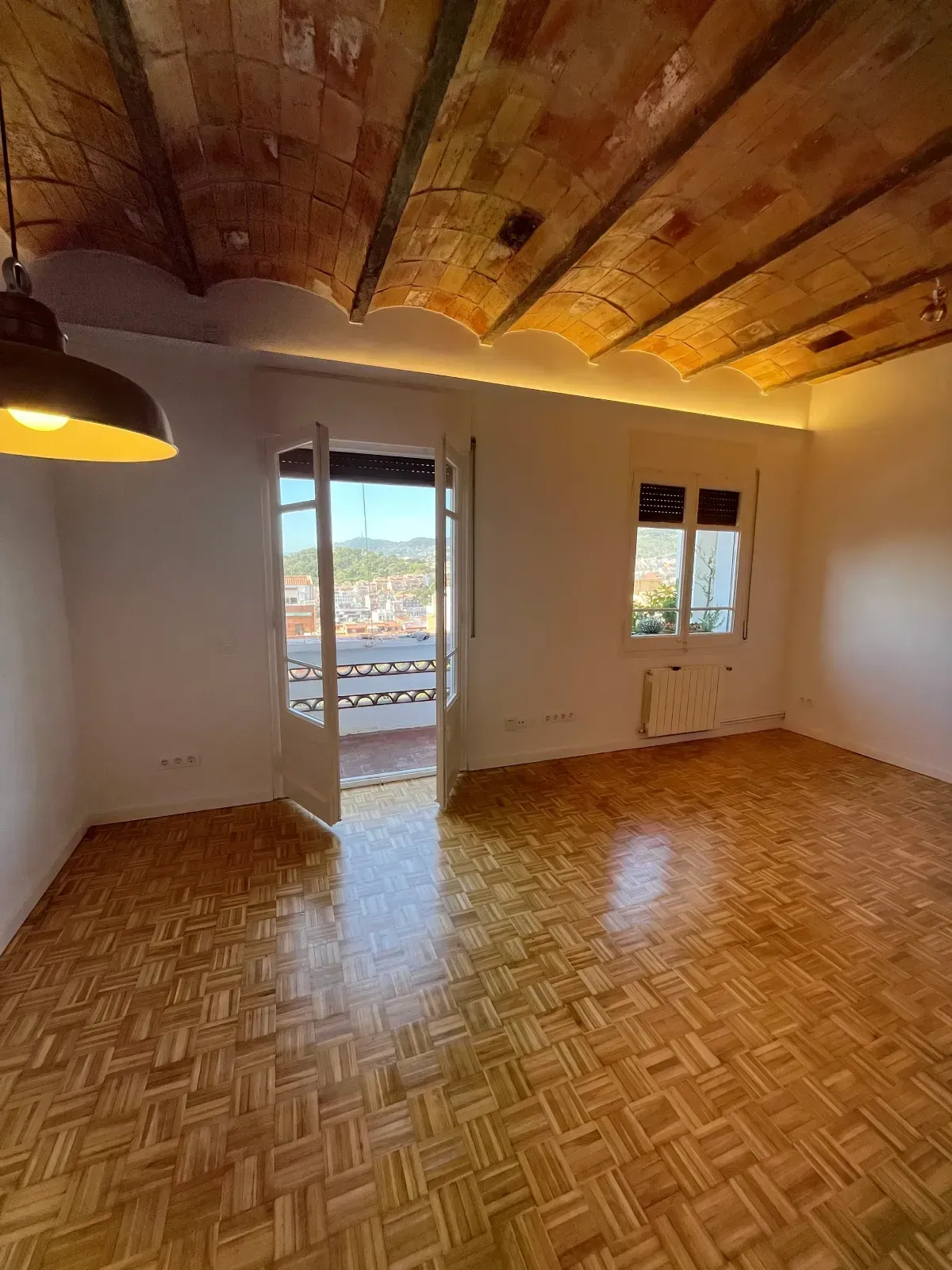 Habitación con techo de madera, puerta balcón, ventana y suelo de parquet.