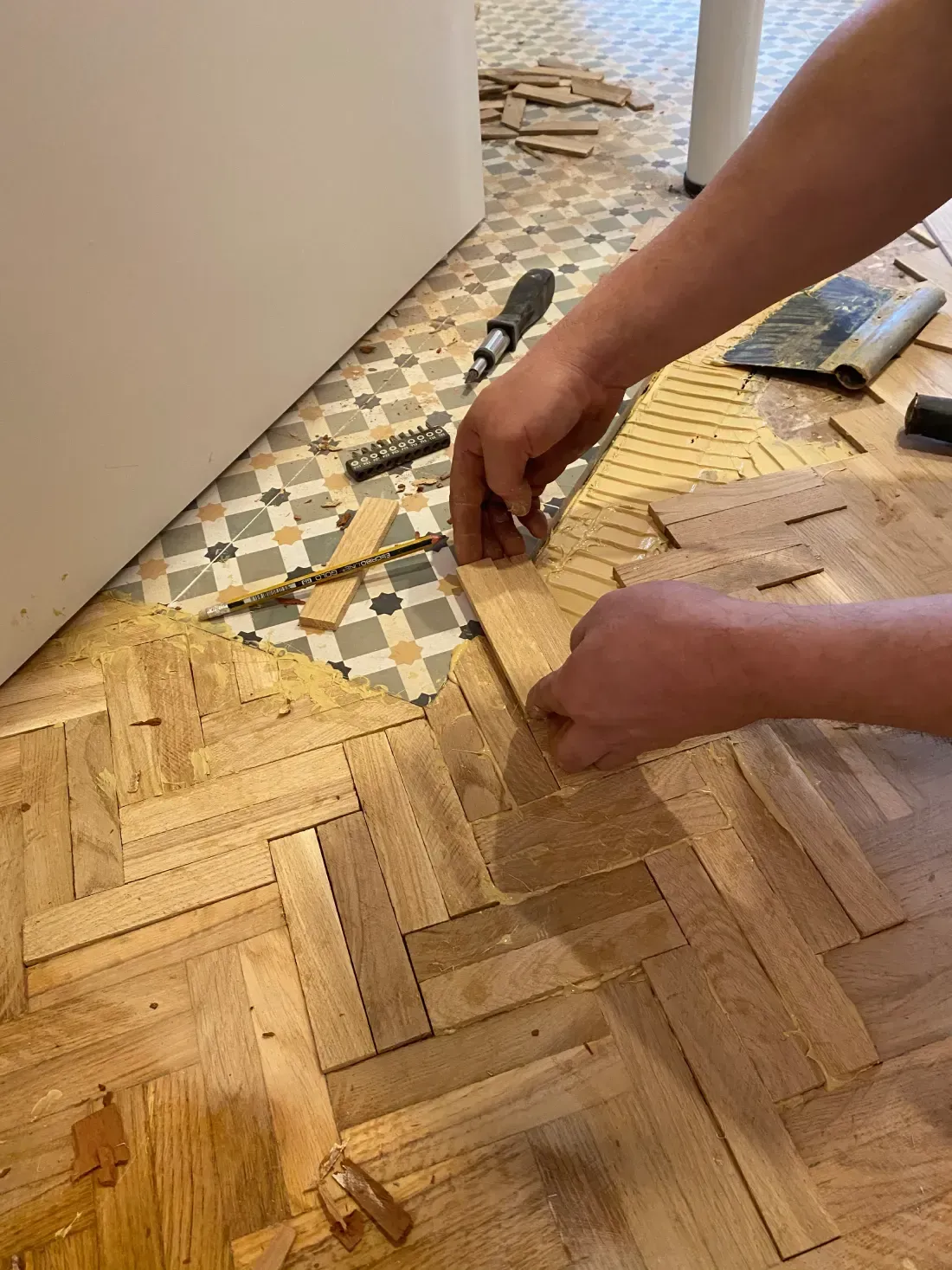 Persona colocando un suelo de parquet de madera, junto a baldosas decorativas, en una habitación.
