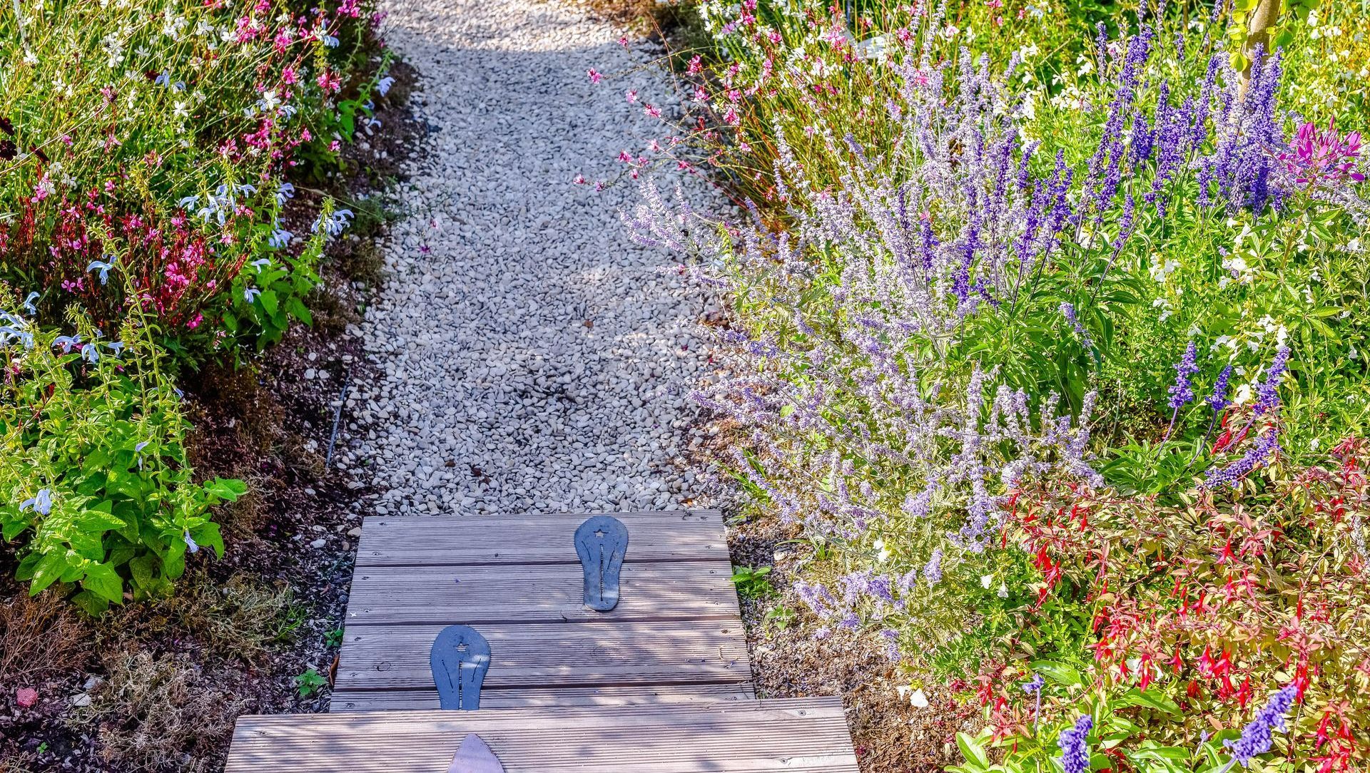 Une allée de jardin en graviers au milieu de deux massifs fleuris