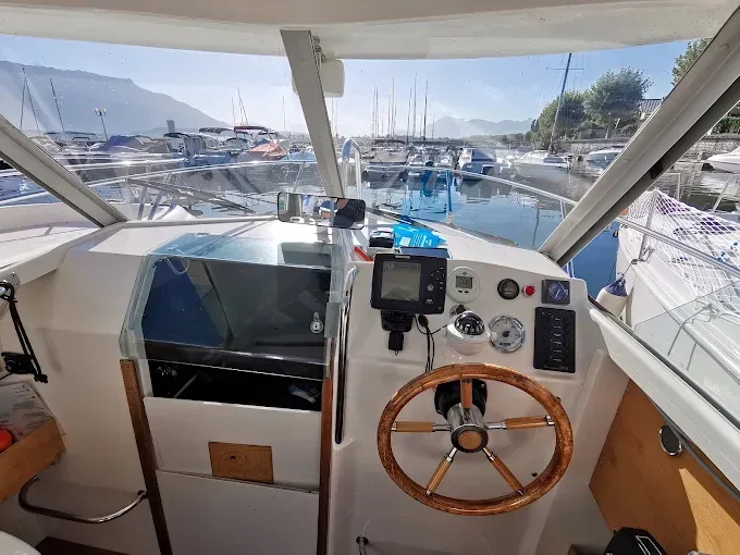 Poste de pilotage d’un bateau-école avec volant, instruments de navigation et vue dégagée sur le port de plaisance et les bateaux amarrés.