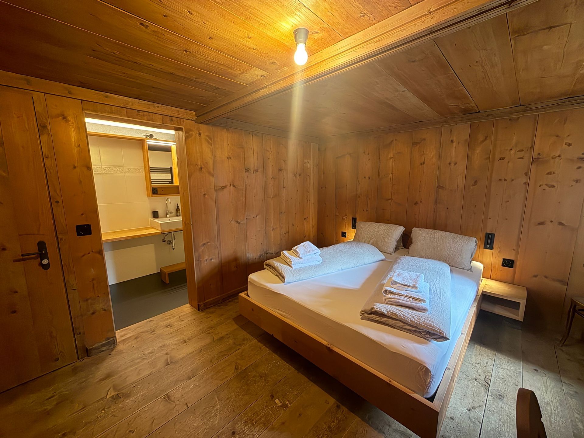 Kleines, rustikales Zimmer mit Sofa, Tisch, Vorhängen und zwei Fenstern, die Licht hereinlassen.